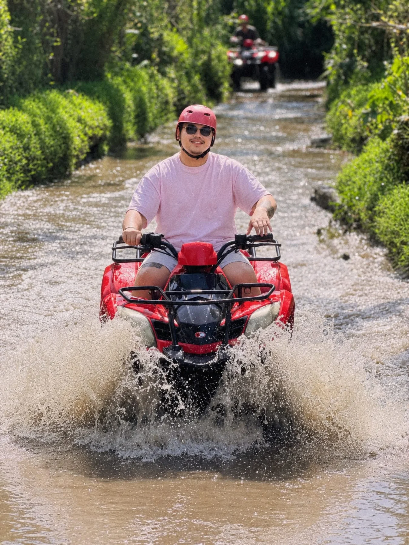 Ean riding a red ATV through a shallow jungle stream